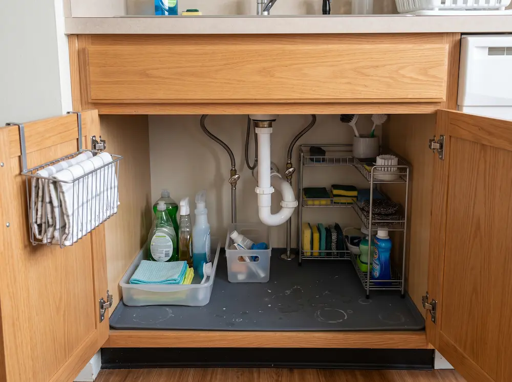 Kitchen sink cabinet with dishwashing supplies, sponges, and cleaning cloths grouped in separate bins
