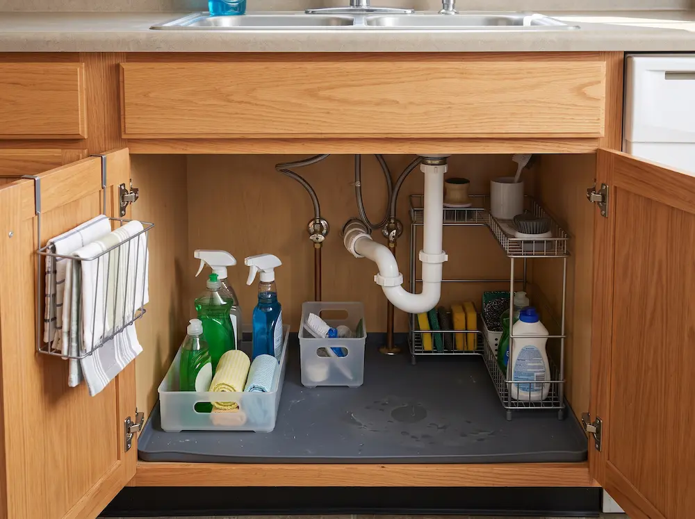 Household cleaning products stored upright in a removable bin under the kitchen sink